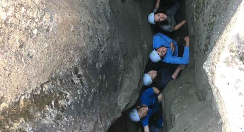 a small group of people smile and look up from a rock crevice 